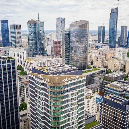 Royal Tulip Warsaw Centre Aparthotel Exterior foto The photo shows a panoramic view of a modern city skyline. In the foreground, there are several tall buildings with contemporary architectural designs. One building prominently features the name "Royal Tulip." The background is filled with numerous s