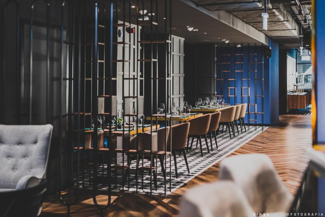 Royal Tulip Warsaw Centre Aparthotel Exterior foto The photo shows a modern restaurant interior. There are multiple dining tables arranged in a long line, each set with tableware and glassware. The space is divided by decorative metal partitions, creating an intimate atmosphere. The flooring features