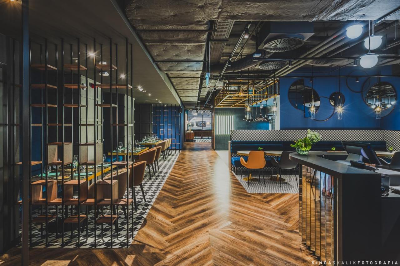 Royal Tulip Warsaw Centre Aparthotel Exterior foto The image shows a modern, stylish restaurant interior. There is a long wooden table with chairs on one side, and a bar area with a shiny counter on the other. The flooring features a herringbone pattern, adding warmth to the space. The walls are pain