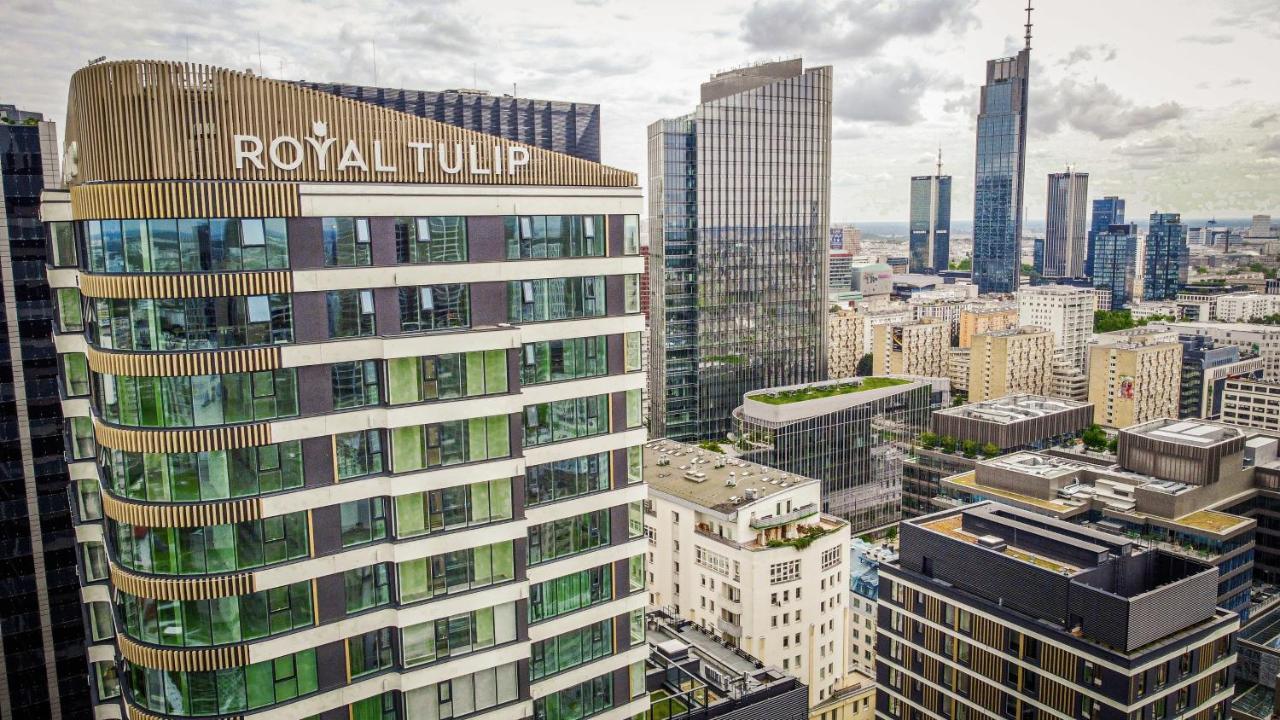 Royal Tulip Warsaw Centre Aparthotel Exterior foto The photo shows a cityscape featuring several modern skyscrapers and buildings. Prominently displayed in the foreground is the "Royal Tulip" hotel, characterized by its contemporary architectural design with large windows. Surrounding it are other ta