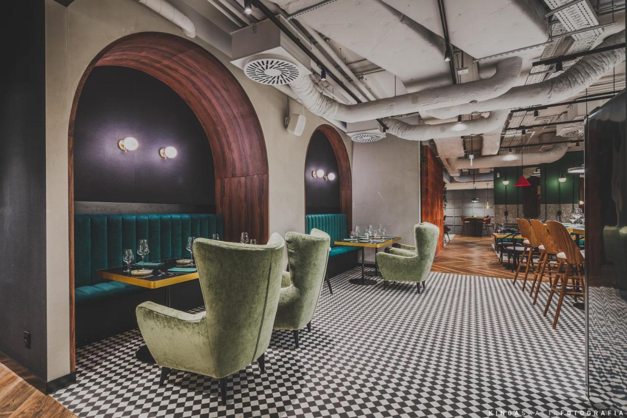 Royal Tulip Warsaw Centre Aparthotel Exterior foto The photo shows a stylish restaurant interior. It features arched openings with warm wood accents and green upholstered seating. The seating includes plush, green armchairs arranged around tables, creating a cozy atmosphere. The floor is decorated wi