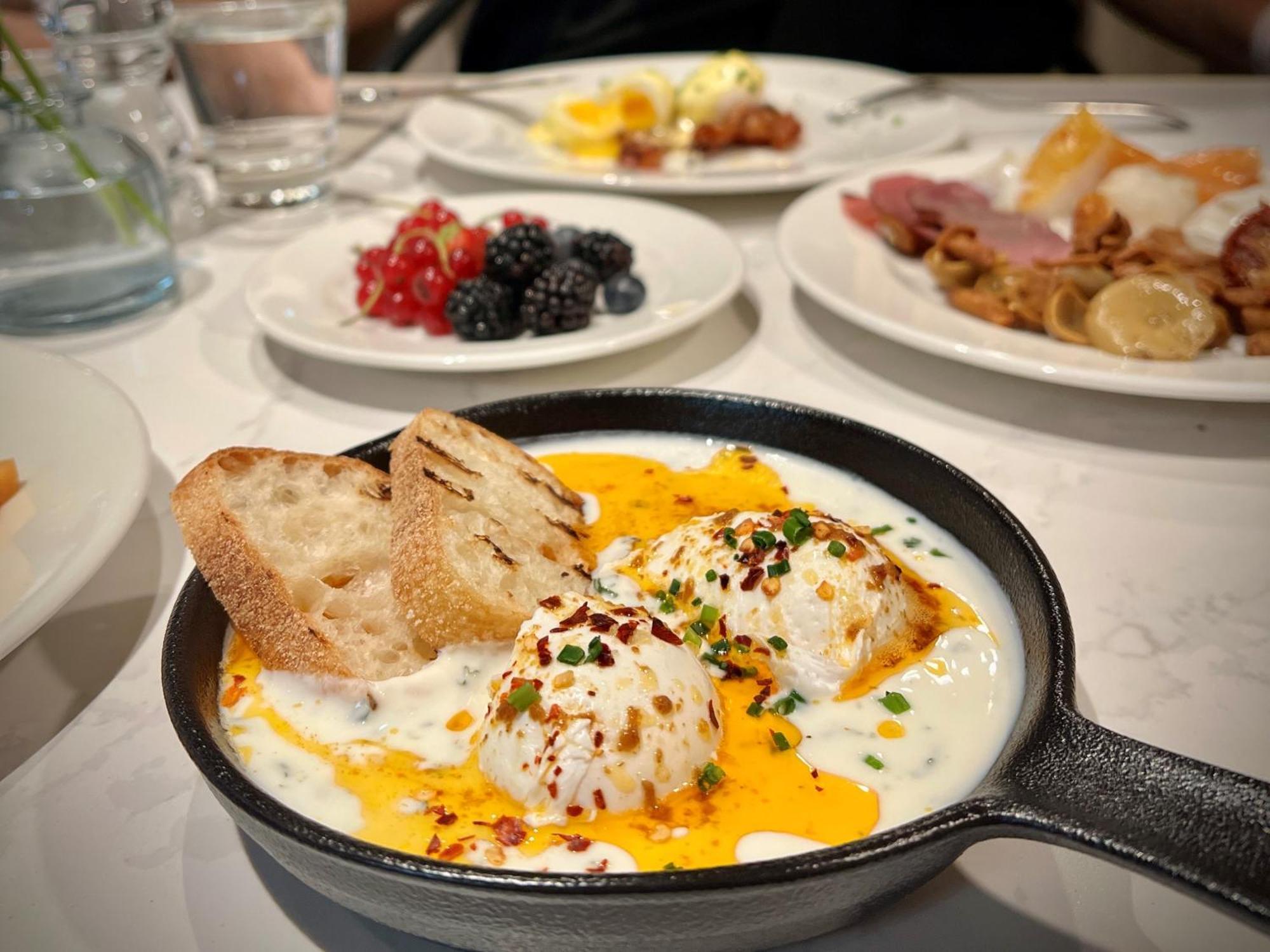 Royal Tulip Warsaw Centre Aparthotel Exterior foto The photo showcases a delicious breakfast spread. In the foreground, there is a cast-iron skillet containing three poached eggs nestled in a creamy sauce, garnished with herbs and red pepper flakes. Next to the skillet, there are slices of toasted br