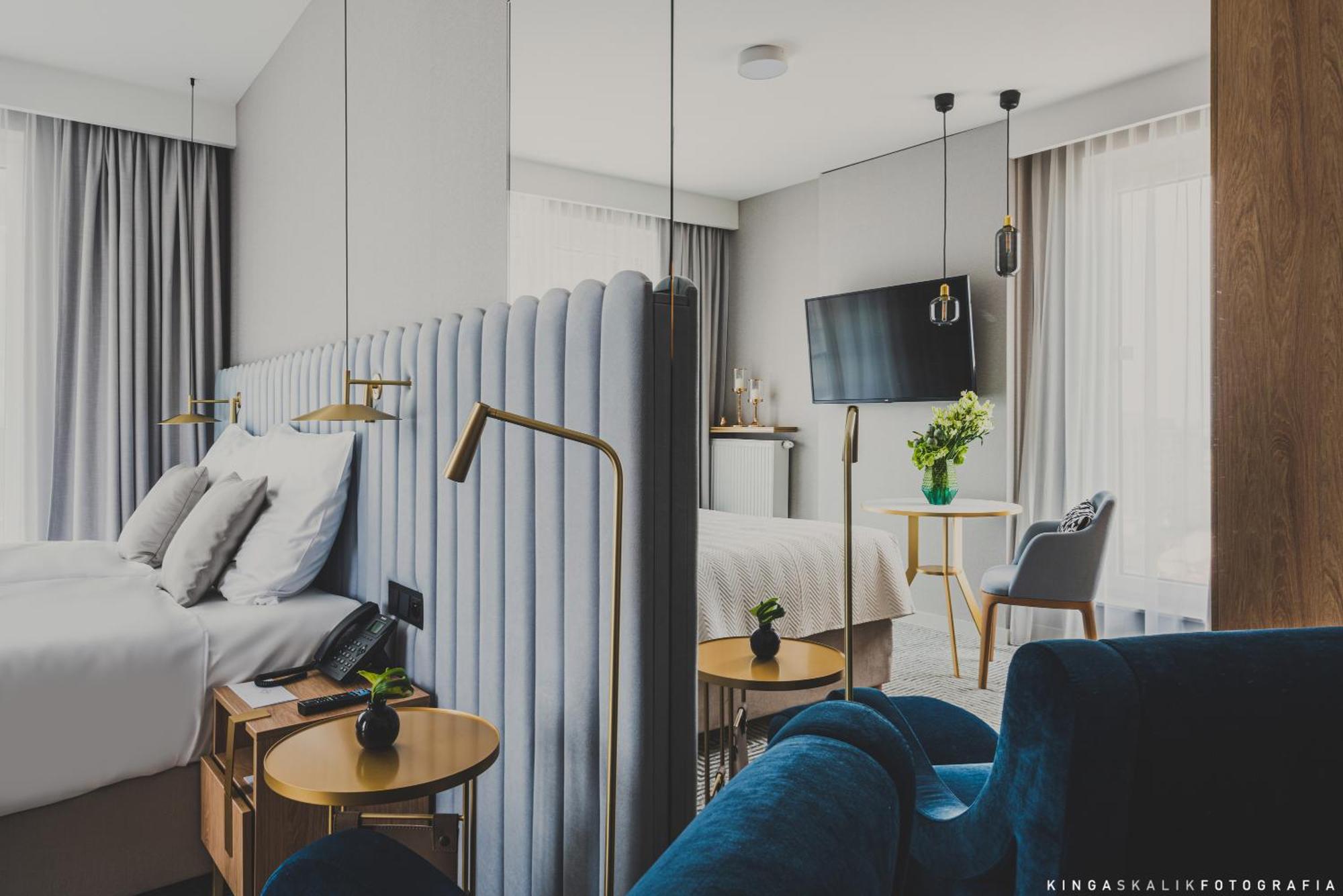 Royal Tulip Warsaw Centre Aparthotel Exterior foto The photo shows a modern hotel room featuring a stylish and contemporary design. In the foreground, there is a bed with a plush, upholstered headboard and white bedding. Beside the bed, there are sleek wooden bedside tables with small plants on top.
