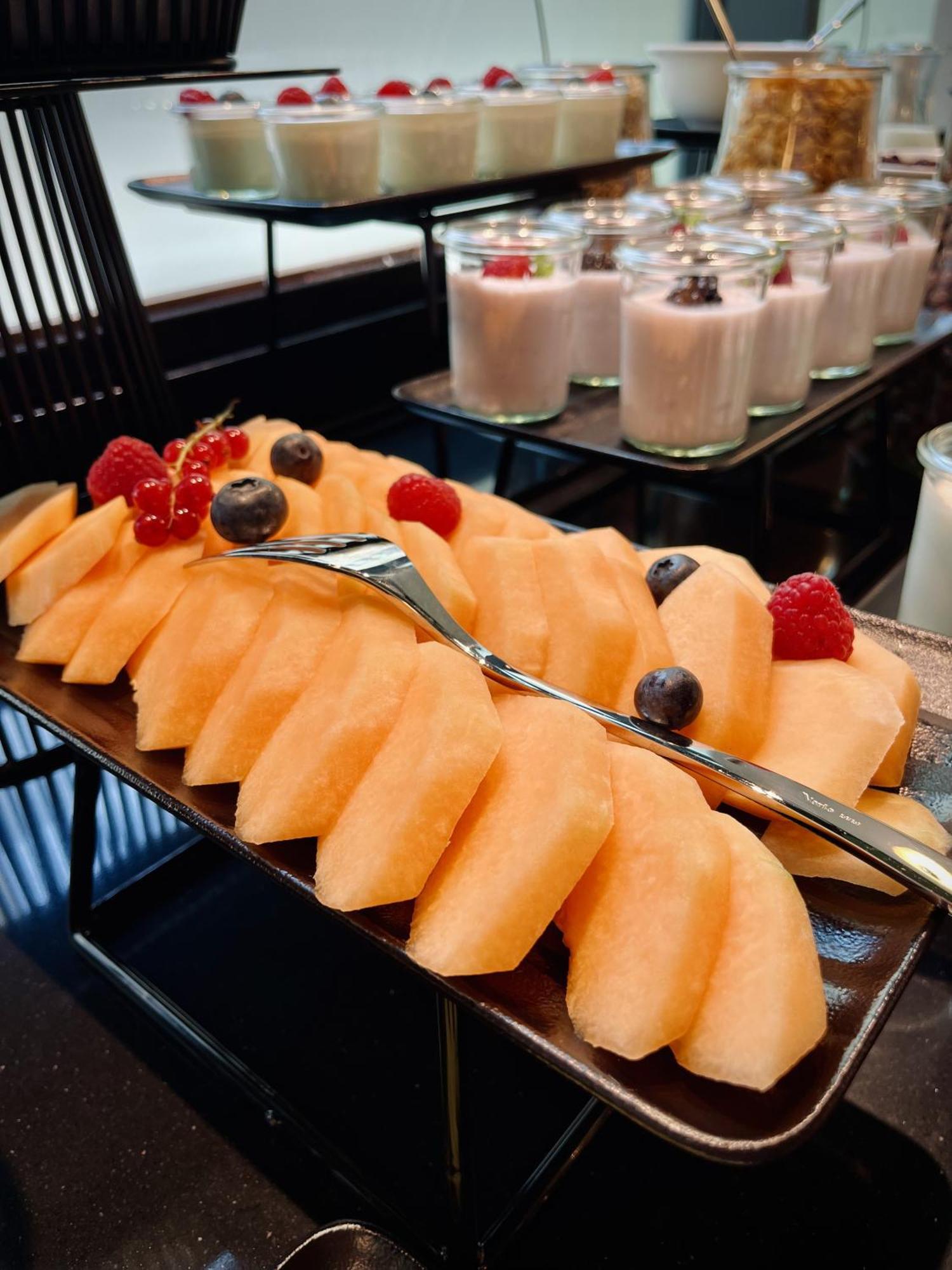Royal Tulip Warsaw Centre Aparthotel Exterior foto The photo features a platter of sliced cantaloupe, arranged neatly and garnished with a few berries. There are red raspberries and blueberries placed on top of the melon slices. In the background, there are cups of dessert, likely some type of puddin