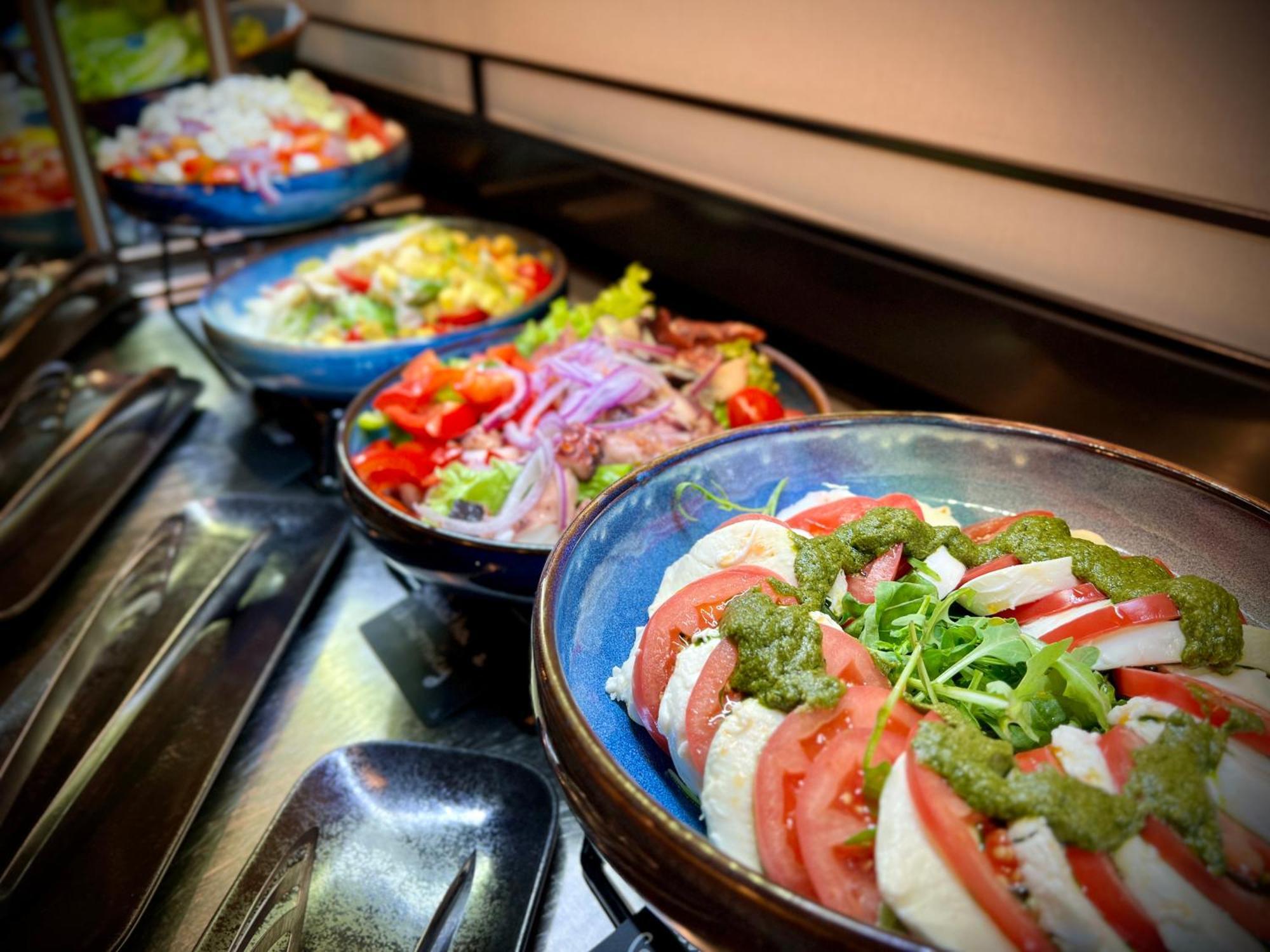 Royal Tulip Warsaw Centre Aparthotel Exterior foto The photo features a variety of dishes arranged in bowls. In the foreground, there is a dish with layers of sliced tomatoes, onions, and a green sauce, likely garnished with herbs or sprouts. In the background, several colorful salads are visible, sh