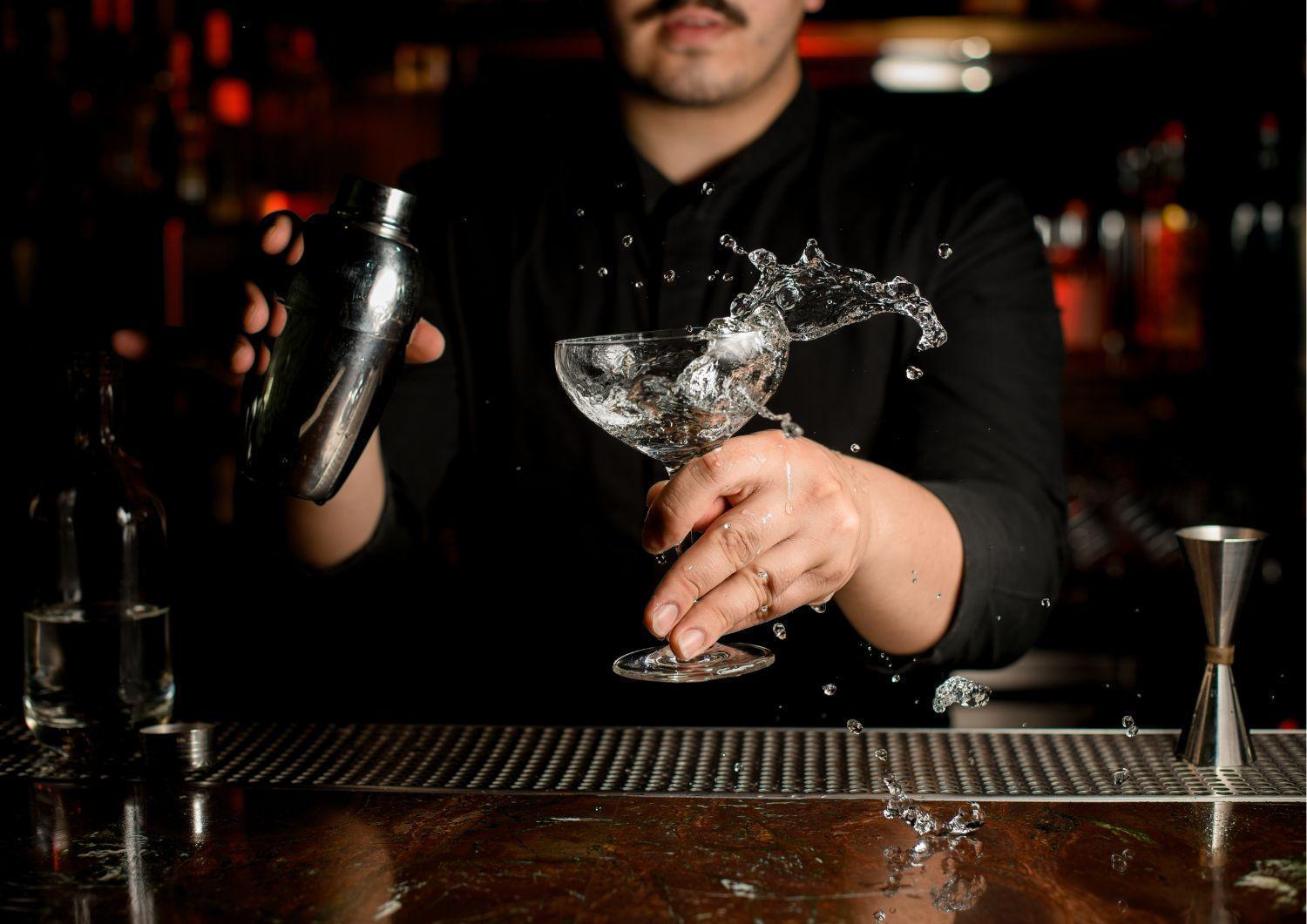 Royal Tulip Warsaw Centre Aparthotel Exterior foto The image shows a bartender in a black shirt shaking a cocktail shaker with one hand. In the other hand, they are holding a glass, likely a cocktail glass, which has liquid splashing out of it. The setting appears to be dimly lit, with blurred lights