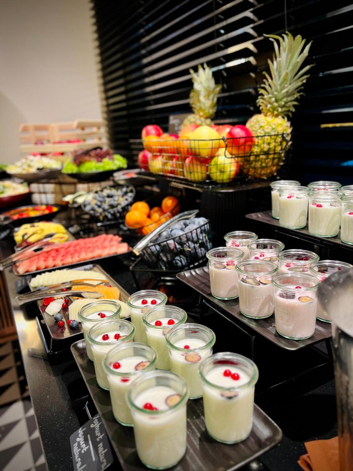 Royal Tulip Warsaw Centre Aparthotel Exterior foto The photo displays an assortment of food items arranged on a buffet table. In the foreground, there are several small glass containers filled with creamy desserts, garnished with red berries. Behind them, various fruits are presented, including apple