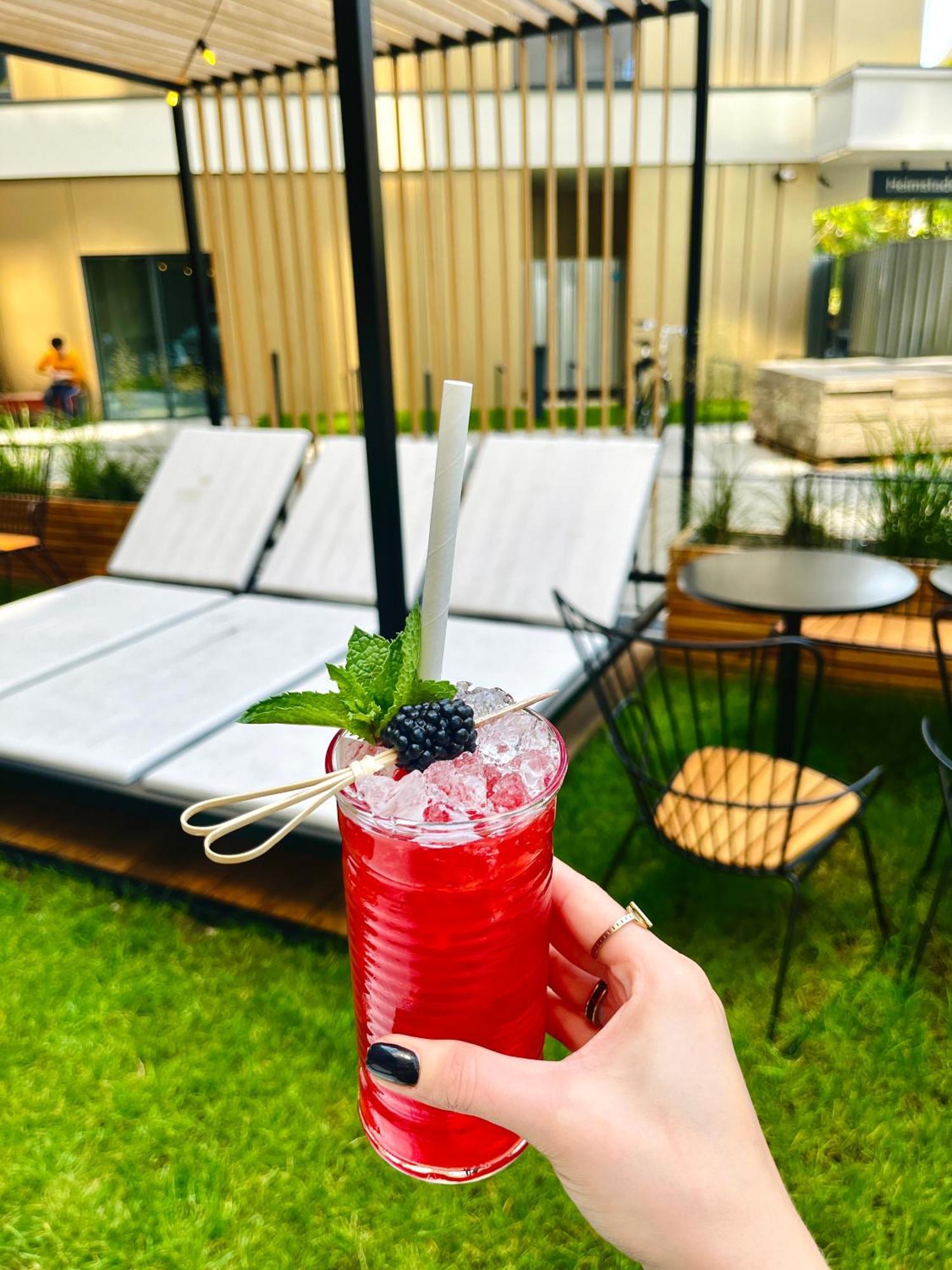 Royal Tulip Warsaw Centre Aparthotel Exterior foto The photo features a vibrant red cocktail served in a clear glass filled with crushed ice. The drink is garnished with a fresh mint leaf and a blackberry, and it has a straw. In the background, there are lounge chairs and a small table, suggesting a 