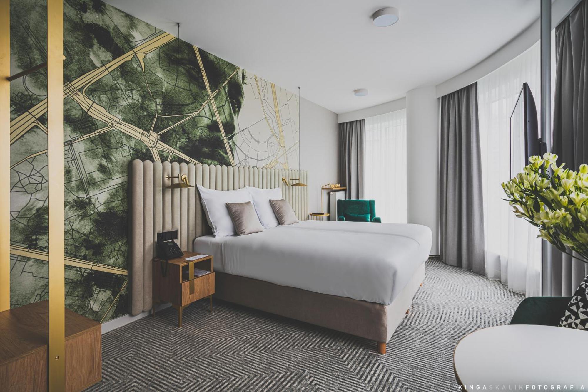 Royal Tulip Warsaw Centre Aparthotel Quarto foto The photo shows a modern hotel room featuring two beds with white bedding. The headboard is upholstered and elegantly designed. Behind the beds, there's a striking wall design with abstract green and gold patterns. The room has large windows with lig